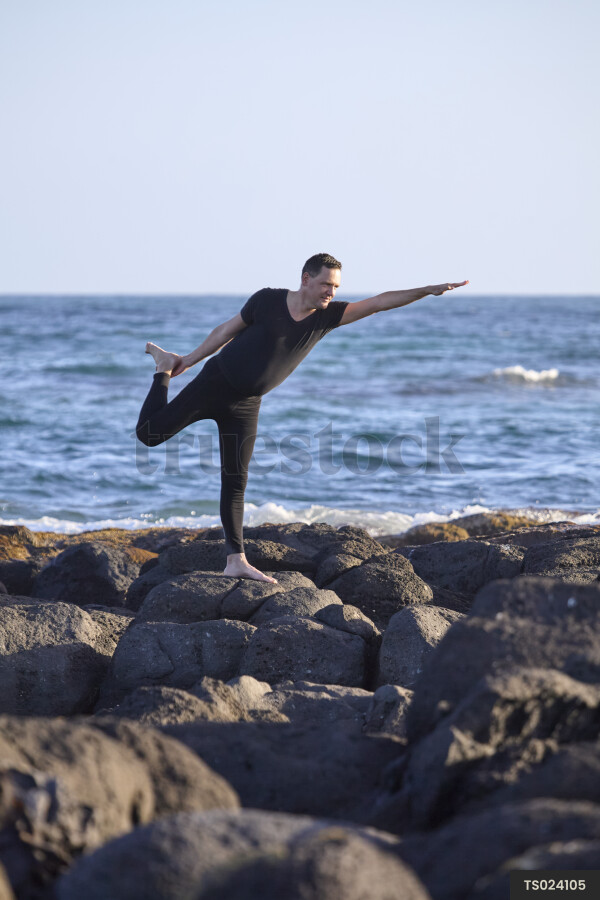 Man doing yoga on rocks at beach
