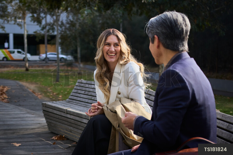 Happy woman talking to man on park bench