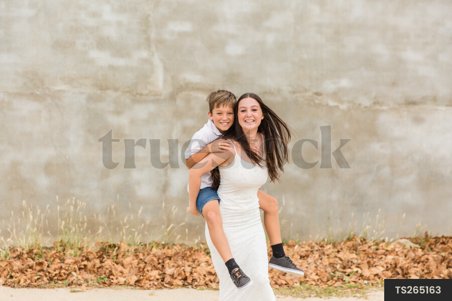 Portrait of sister giving brother piggyback outside