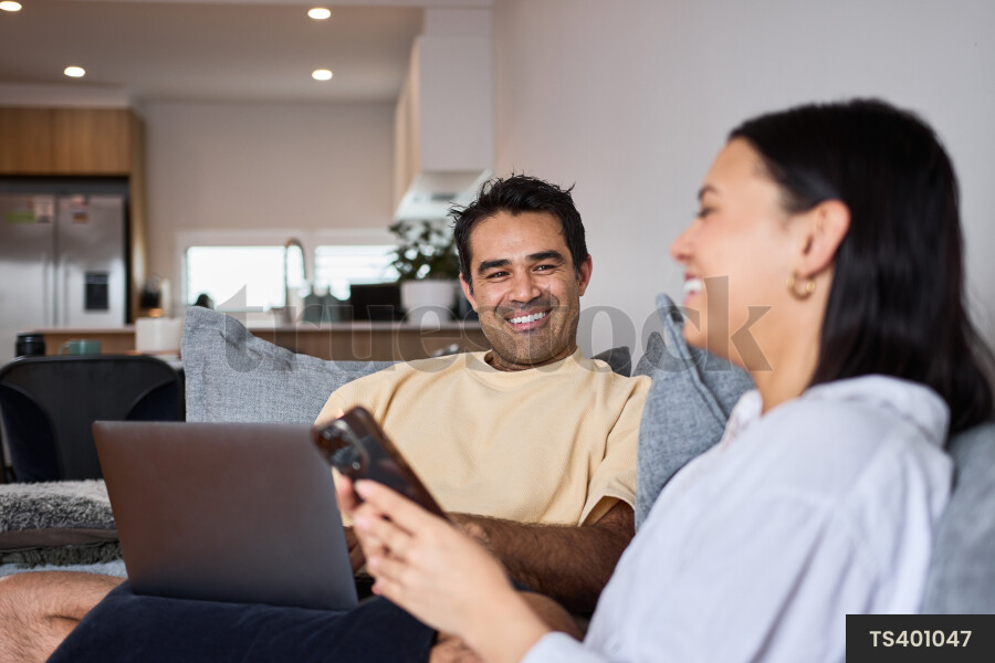 Couple chatting on couch while using digital devices