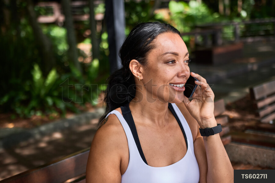 Ethnically ambiguous female sitting on bench using phone at South Bank