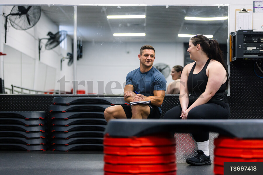 Personal trainer talking with woman in gym by Kathryn Taylor - Truestock