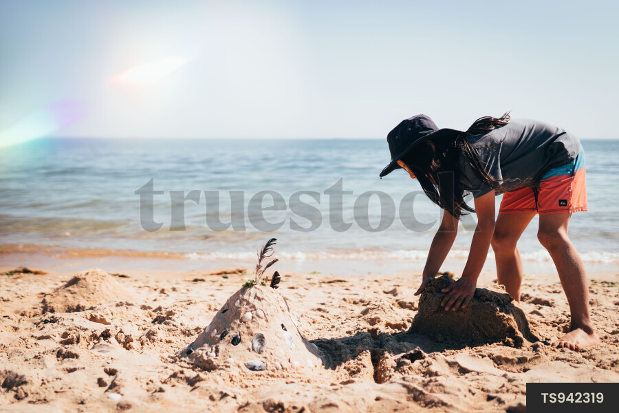 Girl bending over while building sandcastle on beach